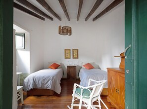 Une chambre avec deux lits, une armoire en bois, une chaise en osier et un luminaire suspendu.