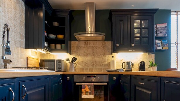 A modern kitchen with dark cabinetry, a stainless steel range hood, a microwave, and an oven. - Elegant & stylish home in historic town centre - Pass the Keys (Moreton-in-Marsh)