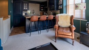 A modern kitchen with dark cabinets, a central island with bar stools, and a leather armchair. - Elegant & stylish home in historic town centre - Pass the Keys (Moreton-in-Marsh)
