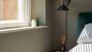 A bedroom with a bed, a nightstand with a lamp, a window, and a view of a building outside. - Elegant & stylish home in historic town centre - Pass the Keys (Moreton-in-Marsh)