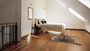 Een slaapkamer met een houten vloer, een zebra-tapijt, een bed met hoofdeinde, een nachtkastje, een ingelijst foto en een dakraam.