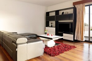 Un salon moderne avec un canapé d’angle, une table basse blanche, un tapis rouge et un meuble de rangement noir pour les appareils électroniques.