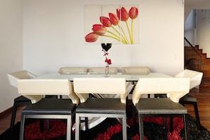Un coin repas avec une table blanche, quatre chaises, un vase de fleurs rouges et un tableau représentant des tulipes rouges accroché au mur.