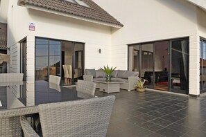 Een moderne buitenruimte met een glazen tafel, rieten meubels en een potplant.