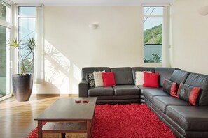 Un salon moderne avec un canapé en cuir, une table basse en bois, un tapis rouge et une grande plante en pot.