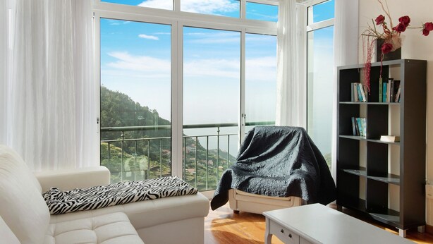 Ein modernes Wohnzimmer mit einem weißen Sofa, einem Zierkissen mit Zebra-Muster, einem schwarzen Sessel mit Decke, einem weißen Beistelltisch und einem Bücherregal.