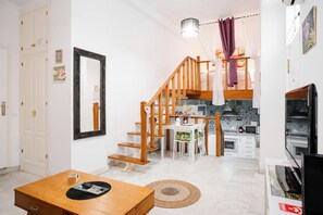 Una cocina moderna con armarios blancos, una escalera de madera y un comedor con mesa y sillas de madera.