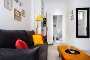 A living room with a sofa, a coffee table, and a lamp. There is a door leading to a bathroom.