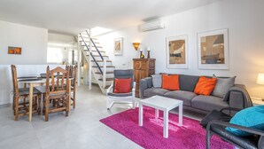 A living room with a dining table, chairs, a sofa, a coffee table, a staircase, and artwork on the walls.
