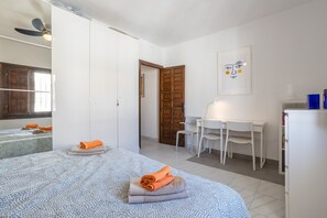 Une chambre à coucher comprenant un lit, deux chaises, un bureau, un ventilateur de plafond et une porte.