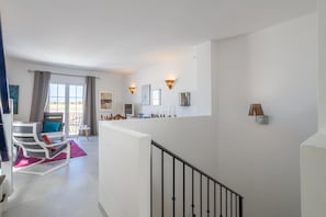 A modern interior with a staircase, a seating area with a sofa and cushions, and a kitchen area with a counter and decorative items.