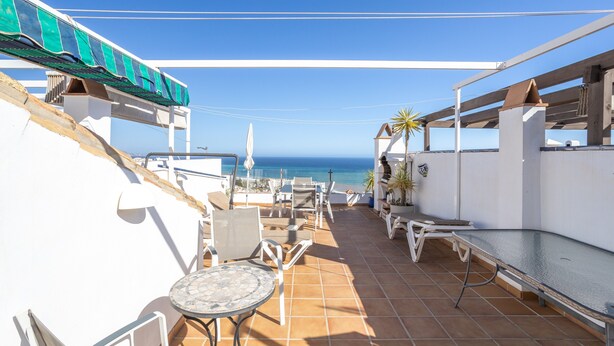 A terrace with outdoor furniture, a view of the sea, and a clear sky.