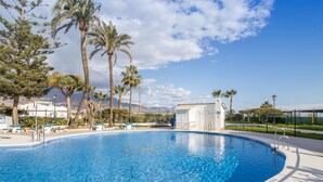 A swimming pool with clear blue water, surrounded by palm trees and a white building.