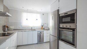 A modern kitchen with stainless steel appliances, a dishwasher, and a window with pendant lights.