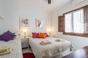 A double room with two beds, a red rug, a wooden table, and artwork on the walls.