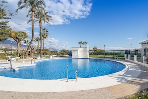 A swimming pool with a white deck, surrounded by palm trees and a clear sky.