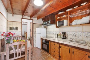 Una cocina con armarios de madera, microondas, lavamanos y comedor con sillas y una mesa.