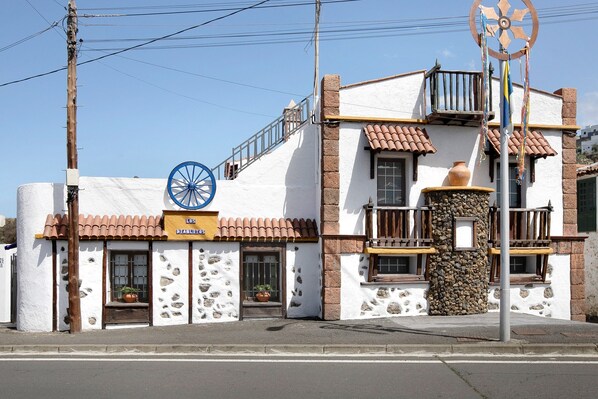 Un edificio con un letrero que dice 'Los Discolores'. Tiene fachada blanca con detalles de piedra, un adorno de rueda azul y un pilar de piedra.
