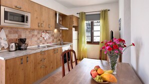 Een keuken met houten kastjes, een magnetron, koffiezetapparaat, spoelbak en een eettafel met een bloevas en fruit.