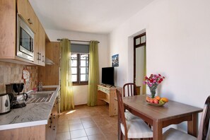 Une cuisine équipée d’un four à micro-ondes, d’un évier et de meubles de rangement en bois. On y trouve une table à manger avec des chaises et un vase rempli de fleurs.