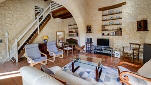 Un salon aux murs de pierre, avec un escalier, des meubles en bois, un téléviseur et une bibliothèque.