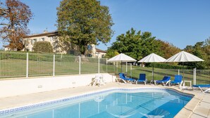 Une piscine aux carreaux bleus, entourée d’une clôture blanche, et des chaises longues bleues.