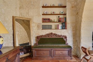 A room with a wooden bench, a mirror, shelves with books and decorative plates, and a tiled floor.