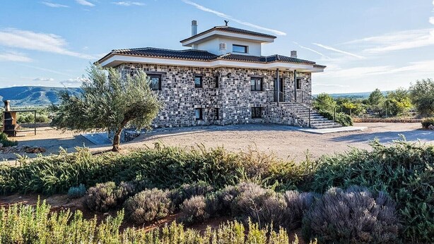 Una casa de piedra con techo de tejas, chimenea y camino de entrada empedrado.