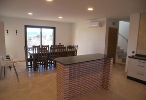 A kitchen with a brick island, wooden dining table, chairs, and a view through a large window. - Villa Casa Rural la Montana 2 with Pool, Garden & Wi-Fi (Chella)