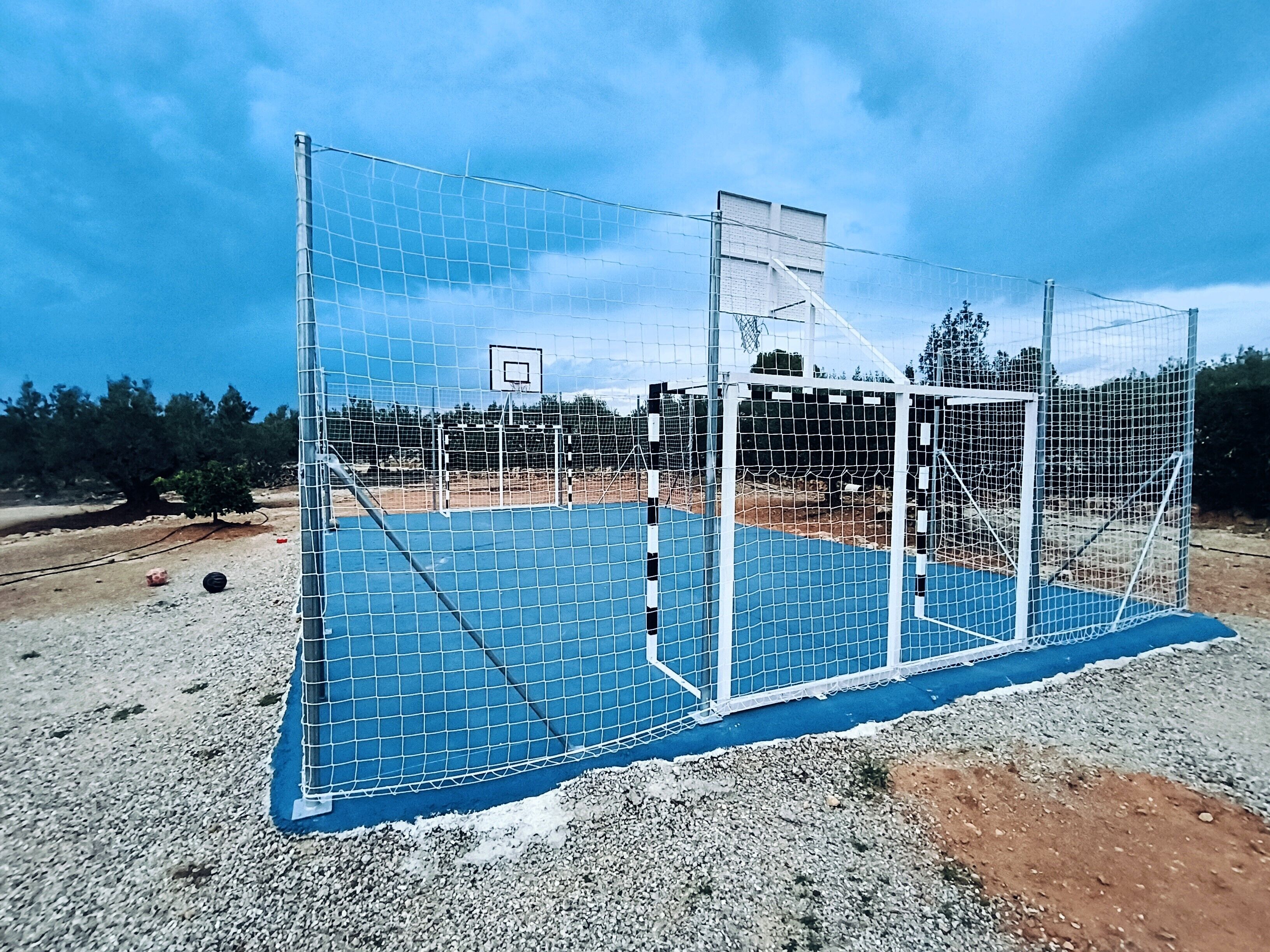Una cancha de baloncesto con superficie azul, un aro de baloncesto y una red de protección.