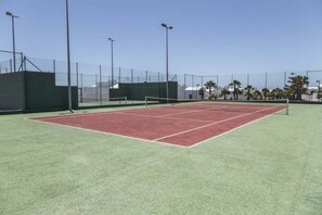 Een tennisbaan met een net, omheind door een hek, en voorzien van verlichting.