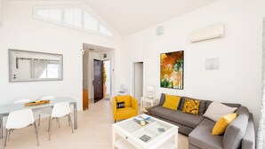 Una sala de estar moderna con un sofá, una mesa de centro y sillas. Hay un comedor con una mesa y sillas. Un espejo grande y obras de arte decoran las paredes.