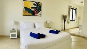 Habitación de hotel con una cama grande, dos mesitas de noche, un velador, una ventana con cortinas y una obra de arte colgada en la pared.