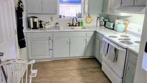 A kitchen with white cabinets, a sink, a stove, and a window with blinds. - COZY- Quiet Cottage Pets Kitchen (Tallahassee)