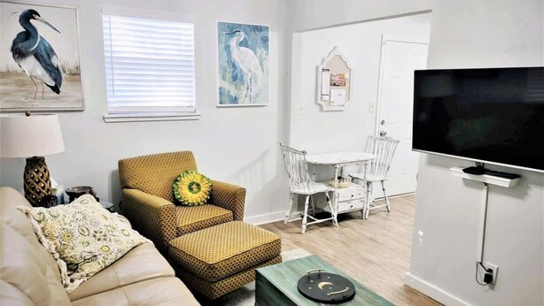 A living room with a sofa, a patterned armchair, a coffee table, a dining table with chairs, a TV mounted on the wall, and artwork on the walls. - COZY- Quiet Cottage Pets Kitchen (Tallahassee)