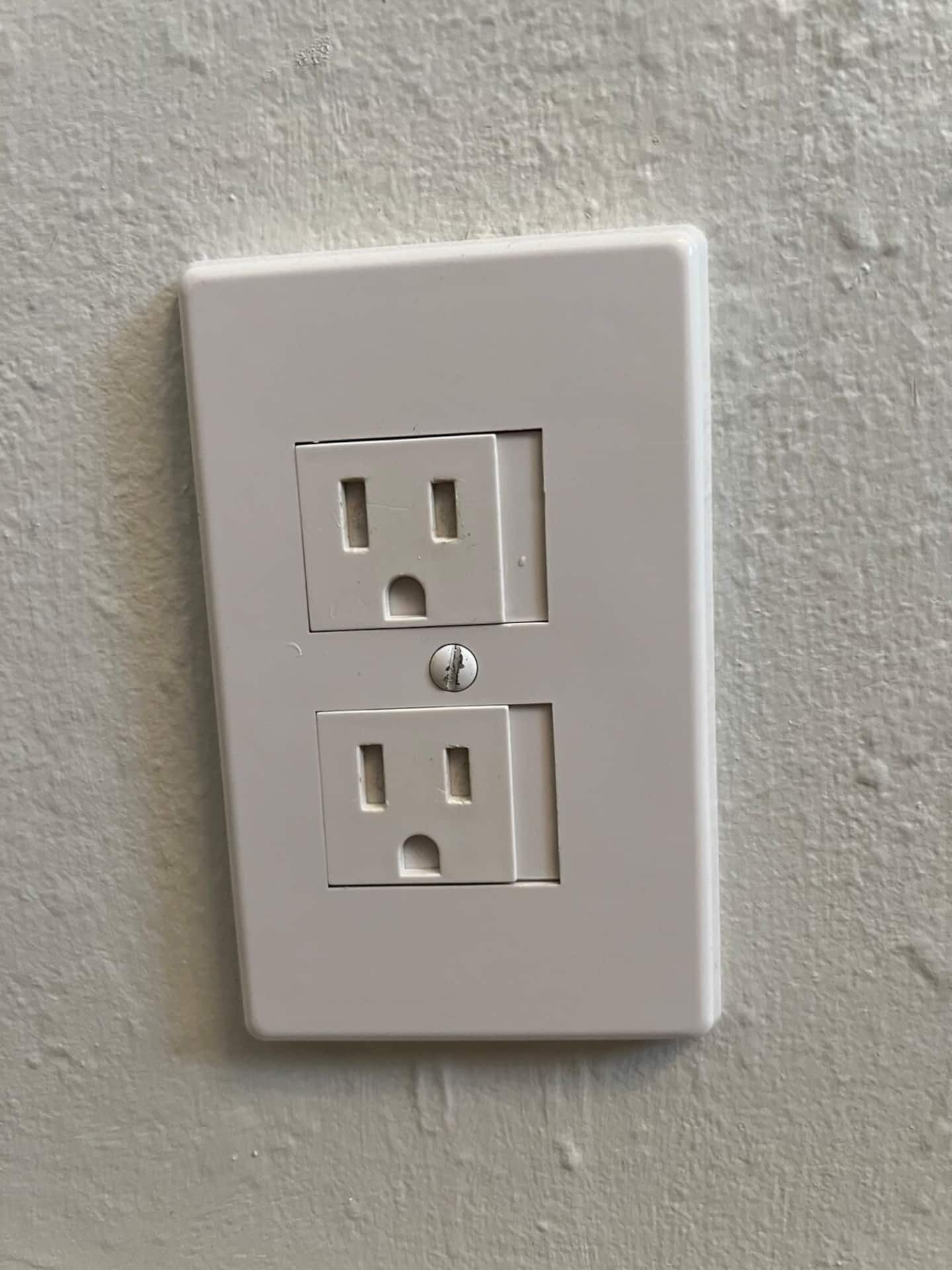 Une prise électrique blanche, dotée de deux fiches et d’un interrupteur, est fixée sur un mur à texture.