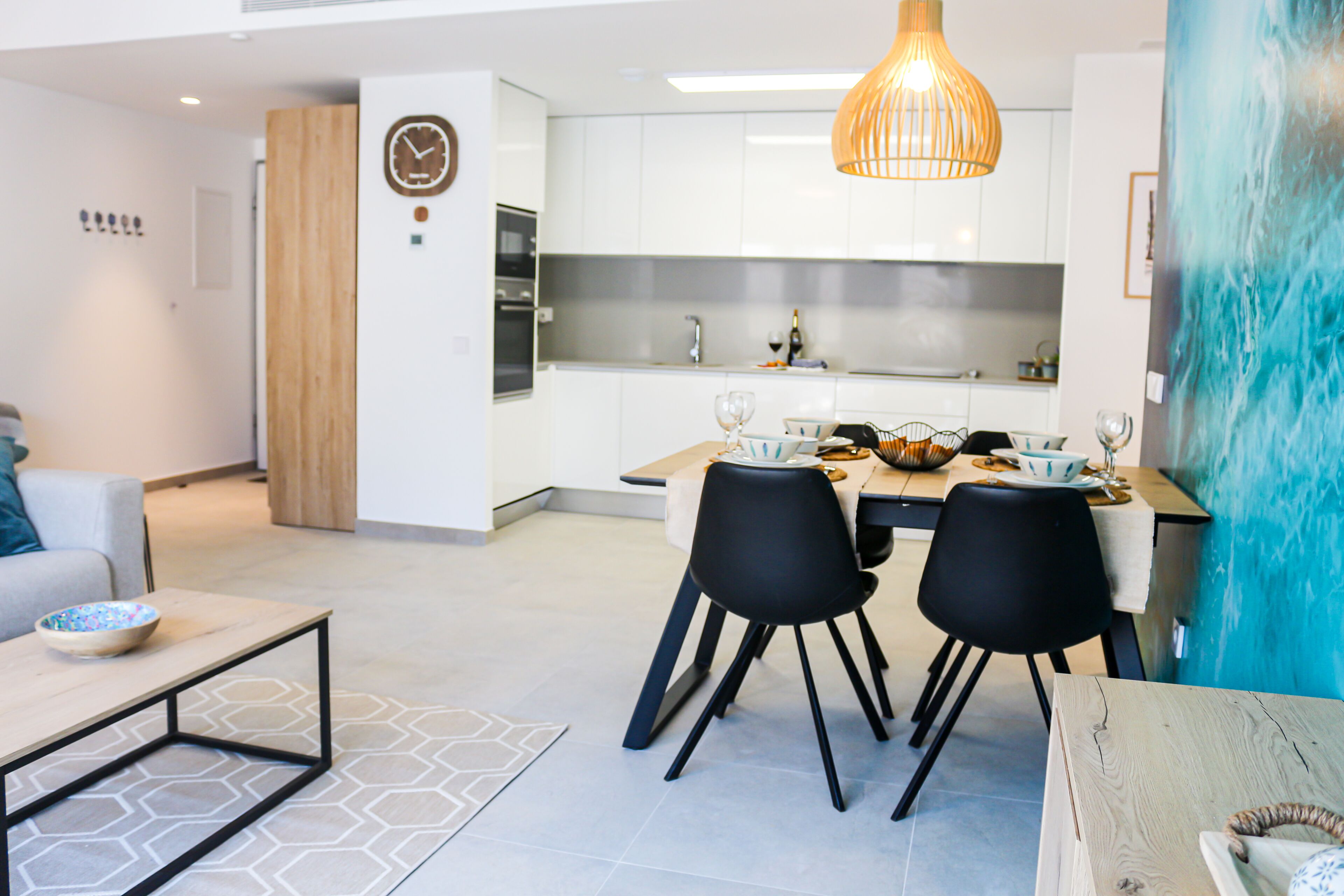 Une cuisine moderne avec des meubles blancs, un coin repas avec des chaises noires et une table en bois.