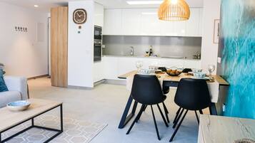 Une cuisine moderne avec des meubles blancs, un coin repas avec des chaises noires et une table en bois.