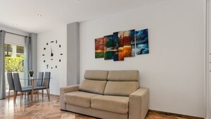 Ein modernes Wohnzimmer mit einem beigen Sofa, einem Glastisch mit Stühlen und einem großen Fenster.