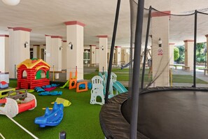 Un espace de jeux pour enfants comprenant diverses structures ludiques, un trampoline et un revêtement de sol en gazon synthétique.