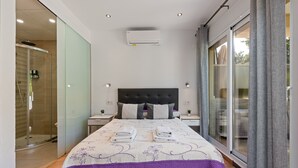 Ein modernes Hotelzimmer mit einem großen Bett, einer Duschkabine aus Glas, einem Flachbildfernseher und einer Schiebeglastür nach draußen.