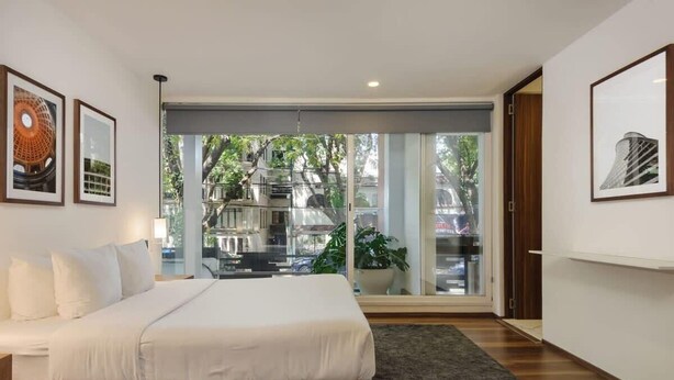 A modern bedroom with a large bed, a view of a cityscape through a sliding glass door, and framed artwork on the walls. - w* | Splendid 1BR with Perfect Balcony in Polanco (Ciudad de México)