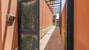 A corridor with a metal gate, a brick pathway, and a building with orange walls. - Holiday Apartment 'Torero II' with Pool, Private Balcony and Wi-Fi (Sevilla)