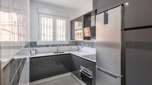 A modern kitchen with a stainless steel refrigerator, a built-in oven, and a window providing natural light. - Holiday Apartment 'Torero II' with Pool, Private Balcony and Wi-Fi (Sevilla)