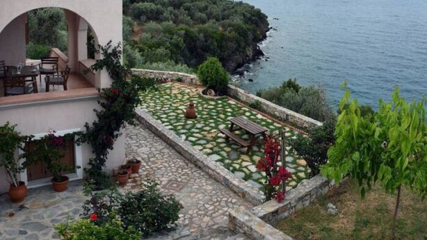 A coastal property with a stone patio, outdoor seating, and a view of the sea and mountains. - Artemis Apartment with Stunning view (Almyros)