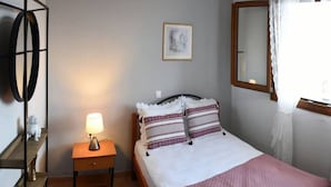 A neatly arranged bedroom with a bed, a nightstand, a lamp, a mirror, and a shelf with decorative items. - Artemis Apartment with Stunning view (Almyros)