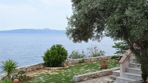 A stone pathway leading to a grassy area with a view of the sea and mountains in the distance. - Artemis Apartment with Stunning view (Almyros)