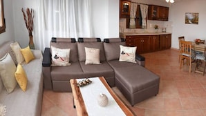 A living room with a sectional sofa, a dining area with a wooden table, and a kitchen with wooden cabinets and a ceiling fan. - Artemis Apartment with Stunning view (Almyros)