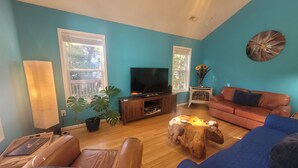 A living room with teal walls, a large window, a TV, a sofa, a coffee table, and a potted plant. - OBX~Beach~Sunsets~Bike Path~Mini Golf~Seafood~Shops~All within 1/2 mile away (Kill Devil Hills)