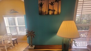 A room with a wooden coffee table, a lamp, a small palm tree decoration, and a painting of palm trees on the wall. - OBX~Beach~Sunsets~Bike Path~Mini Golf~Seafood~Shops~All within 1/2 mile away (Kill Devil Hills)